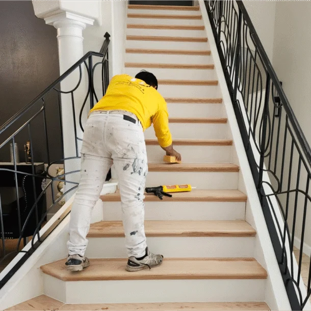 Professional painter from United Painting homes meticulously applies finishing touches to white and wood interior stairs.